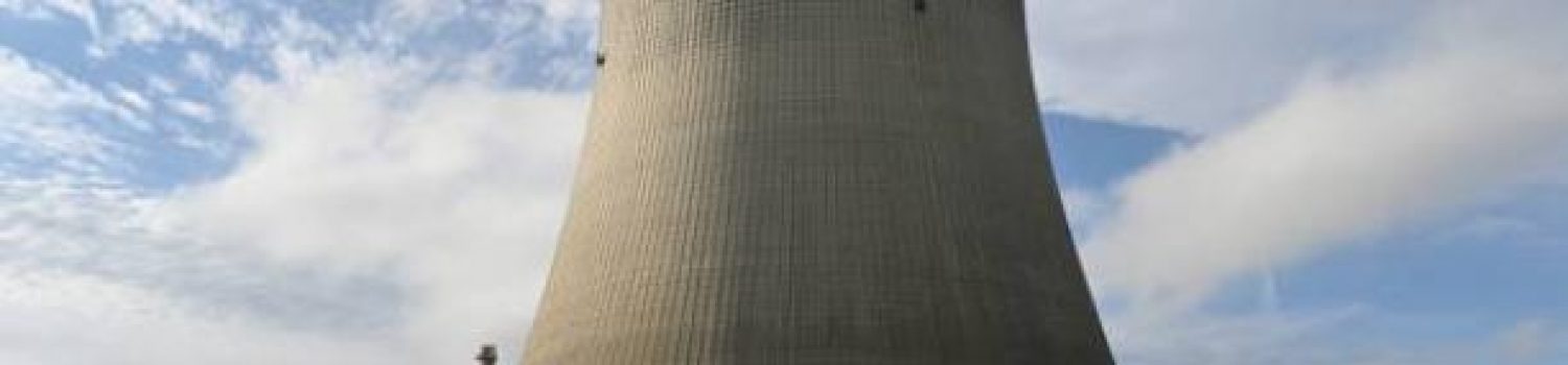 A large cooling tower at a nuclear power plant under a partly cloudy sky.