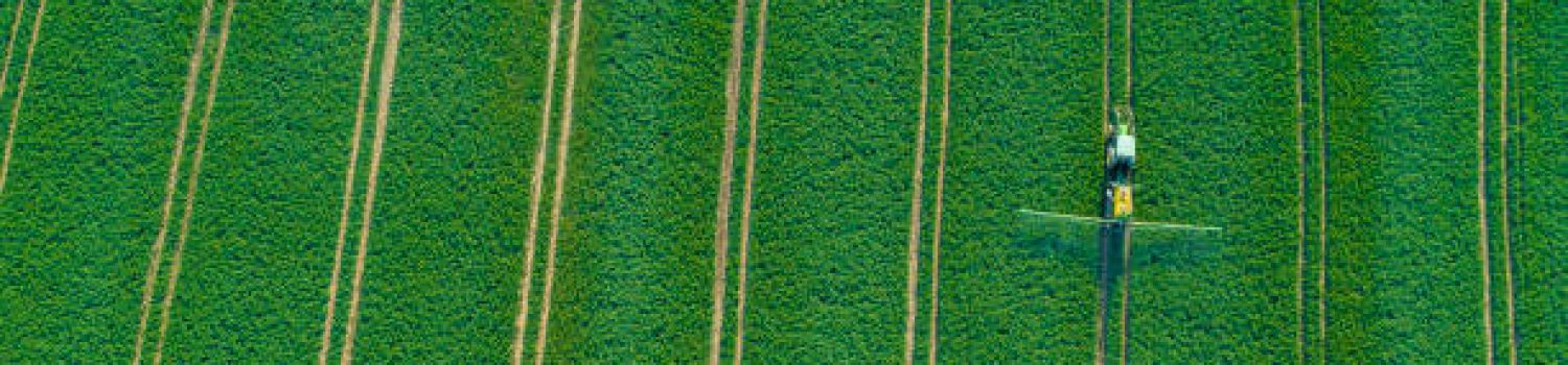 Aerial view of a tractor fertilizing a cultivated agricultural field.